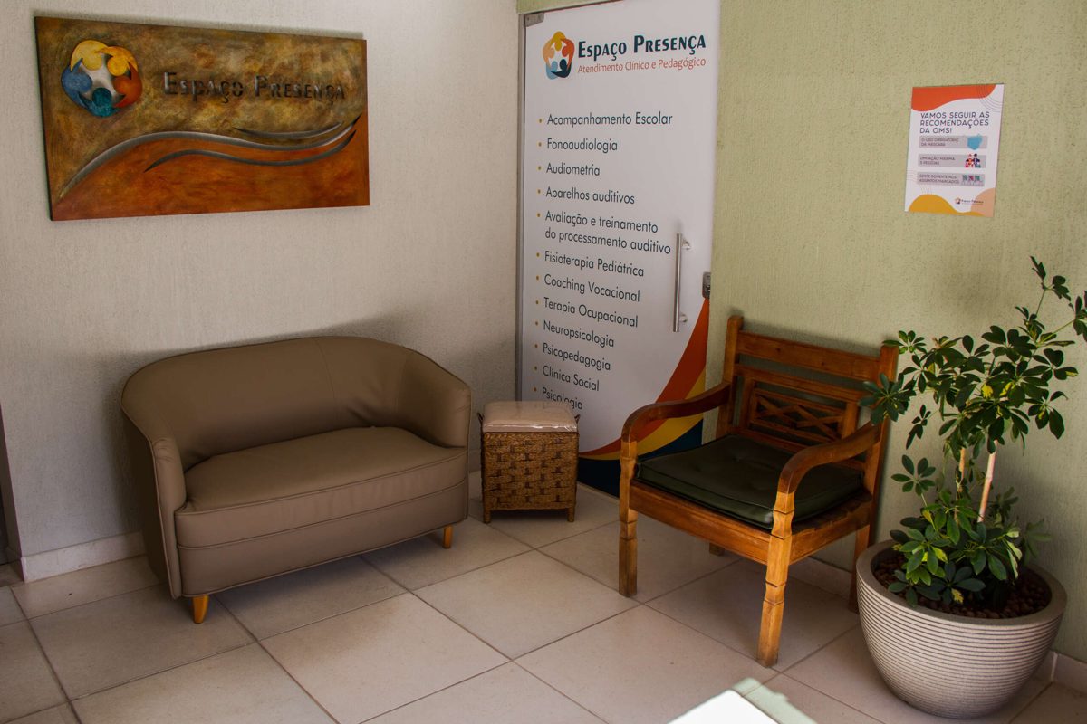 Recepção do Espaço Presença, com sofá, poltrona e a placa da clínica na parede