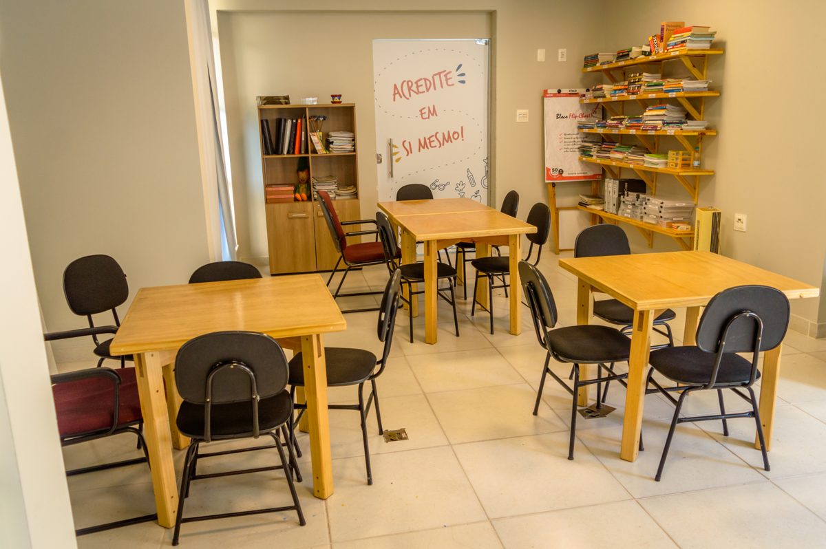 Sala de estudos com mesas de madeira e a frase Acredite em si mesmo na parede